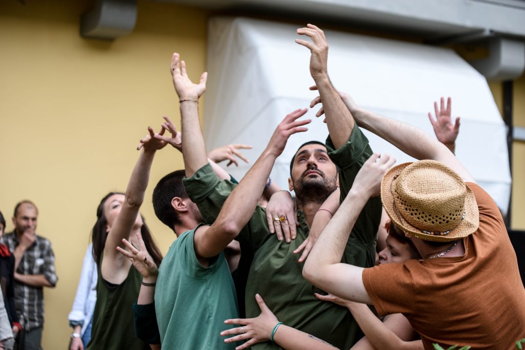 Some boys and girls during an outdoor performance, in a group, with arms raised to the sky and intertwined.