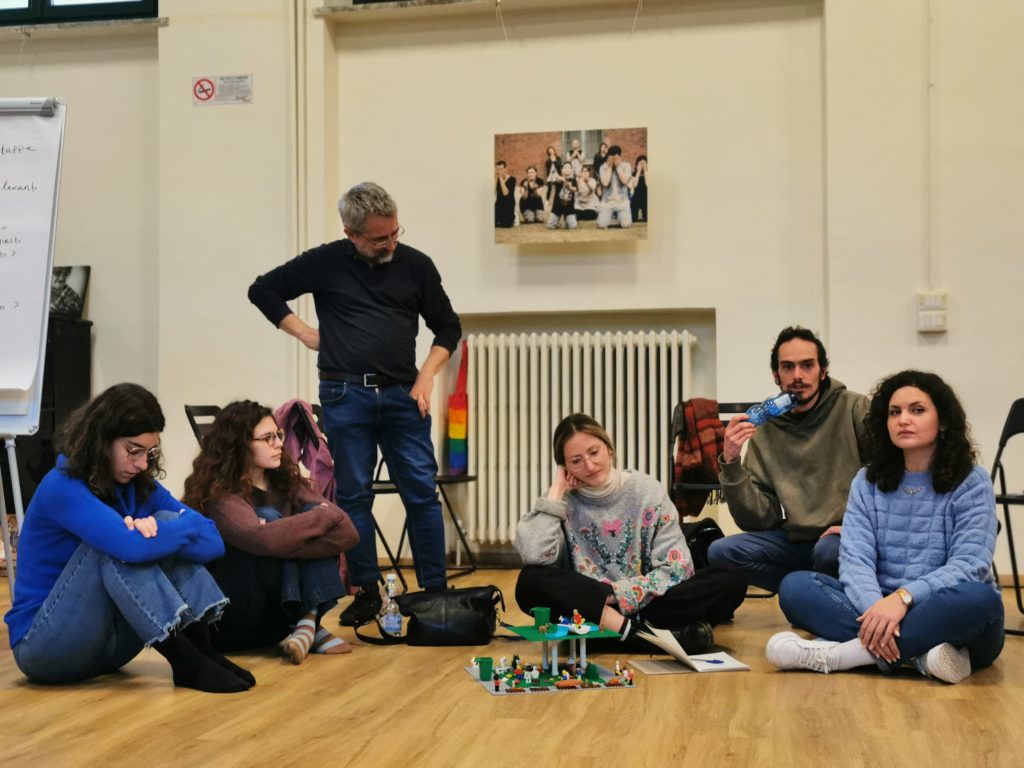 Some people during the course, sitting on the ground, with a Lego construction in front of them.