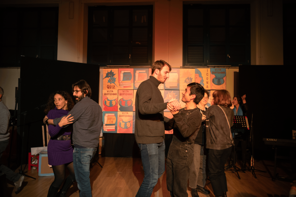 Varie persone sul palco durante lo spettacolo che ballano in coppia. Dietro di loro le caselle del gioco dell'oca