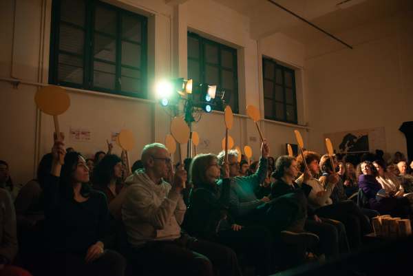 Foto del pubblico durante lo spettacolo con in mano delle palette giallo mentre votano