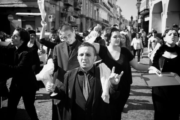 Black and white photo of the crowd during a street event. The people in the foreground have champagne glasses in their hands and wave white cloth handkerchiefs