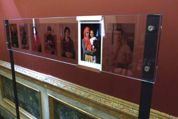 An exhibition of photographs hanging on a wall inside a museum, depicting people of different cultures, ages, and backgrounds.