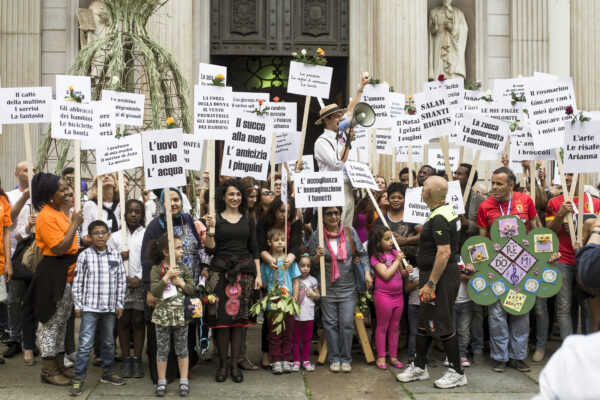 A crowd at a parade, in a group, of different ages and cultures, each holding a wooden pole with a sign at the end with writing on it. In the center, an SCT worker with a megaphone.