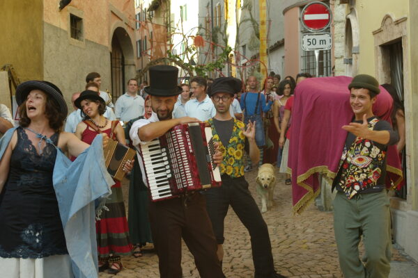 Crowd in the street during a parade event. In the front row SCT performers, actors, actresses and musicians playing the accordion