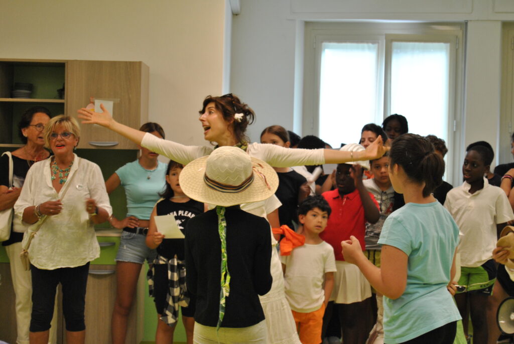 Attrice vestita di bianco canta coinvolgendo gli e le ospiti della RSA