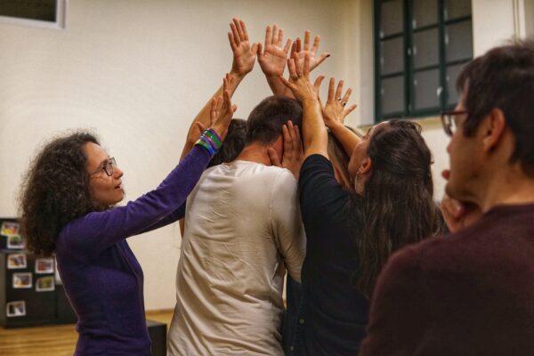 A group of participants in the OnStage workshop, gathered in a tight circle, with their hands raised over the head of one participant in the middle of the circle.